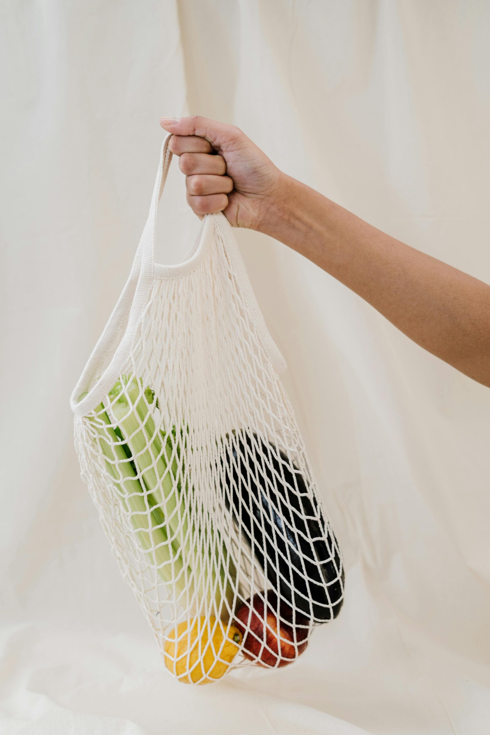 Hand holding a reusable mesh bag filled with colorful fresh vegetables, promoting zero waste lifestyle.